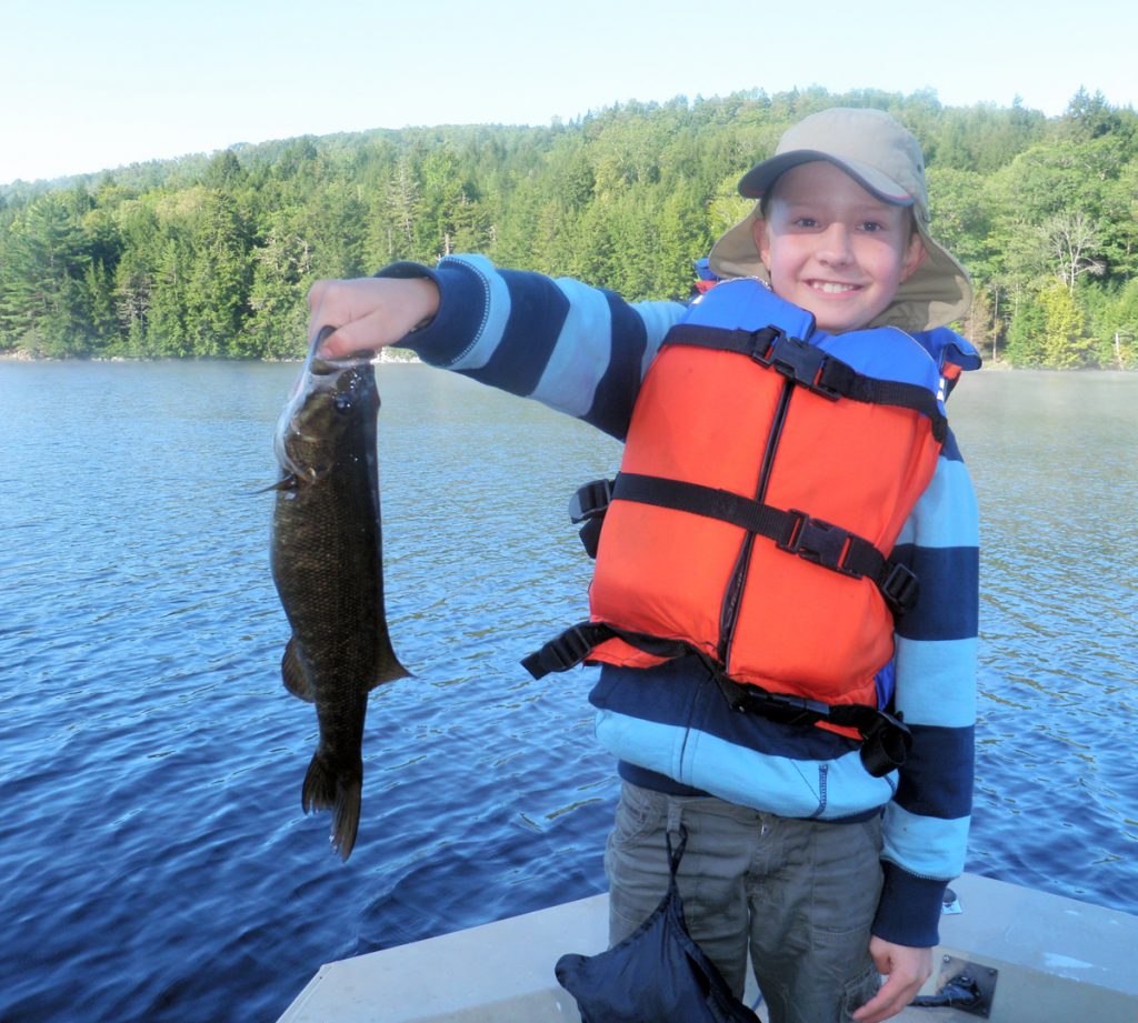 Kid holding a fish he caught on a lake in Maine - Northern Outdoors