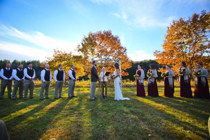 Maine wedding ceremony with full bridal party and blue sky with fall leaves