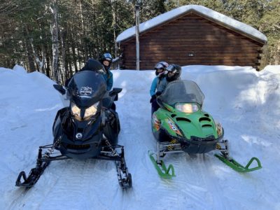 Couples Snowmobile from a Trailside Cabin