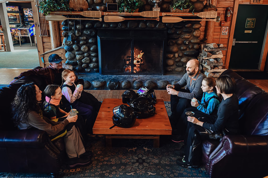 Family enjoying drink in front of stone fireplace at the kennebec river brewery.