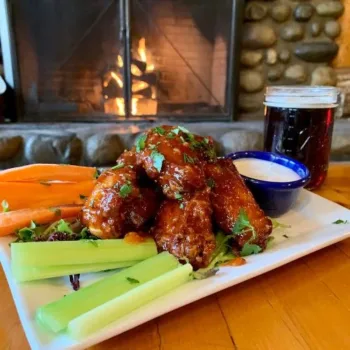 Wings in housemade sauce with a pint of beer in front of fireplace.