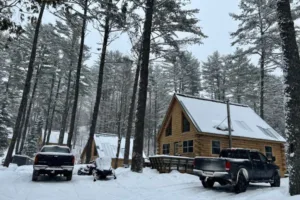 Cabin in snow with truck and trailer and snowmobile